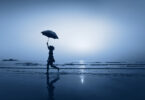 Mulher andando de guarda-chuva na praia à noite.