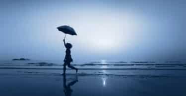 Mulher andando de guarda-chuva na praia à noite.