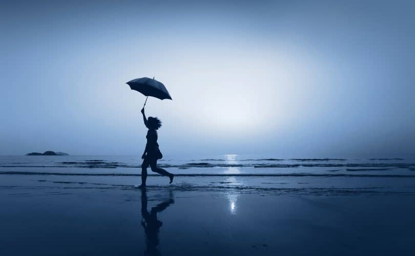Mulher andando de guarda-chuva na praia à noite.