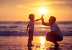 Pai e filho tocando as mãos em praia.