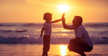 Pai e filho tocando as mãos em praia.