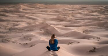 Mulher sentada de costas em deserto de areia