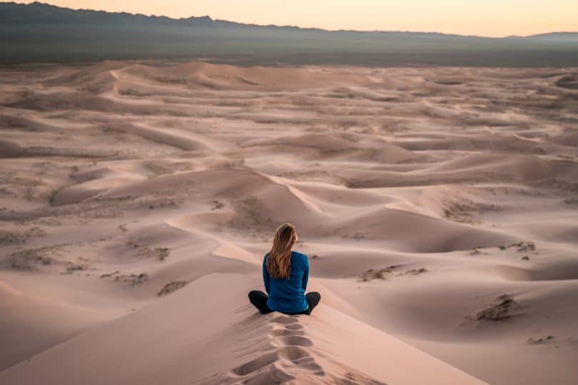 Mulher sentada de costas em deserto de areia