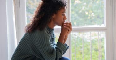 Mulher negra sentada perto de janela, refletindo sobre a vida