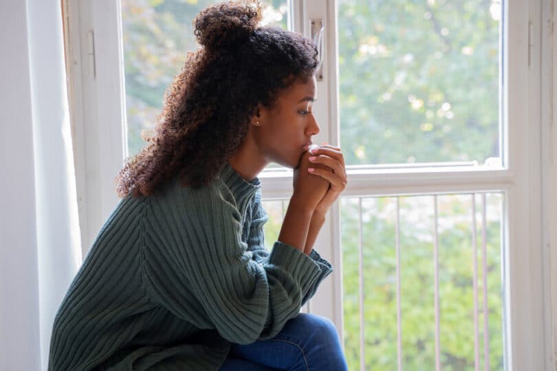 Mulher negra sentada perto de janela, refletindo sobre a vida