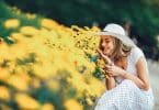 Mulher jovem sorrindo ao lado de um canteiro de flores amarelas.