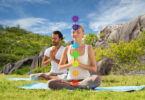 casal meditando na posição de lótus com sete símbolos de chakra sobre fundo de natureza