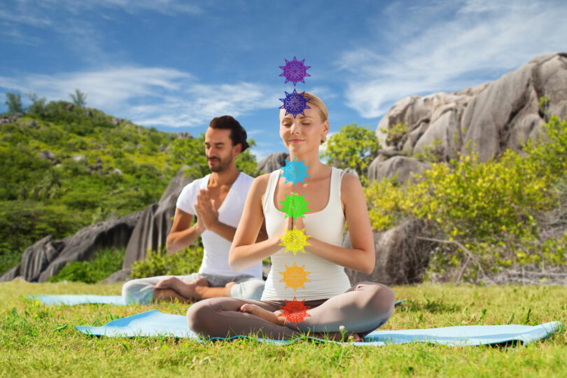 casal meditando na posição de lótus com sete símbolos de chakra sobre fundo de natureza