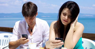 Casal tomando café da manhã cada um com seu celular