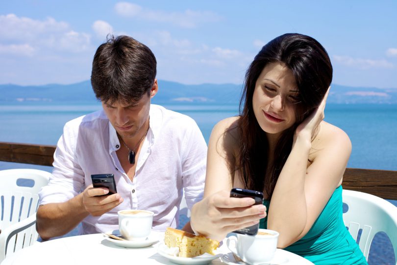 Casal tomando café da manhã cada um com seu celular