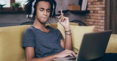 Homem ouvindo música de fone com laptop no colo