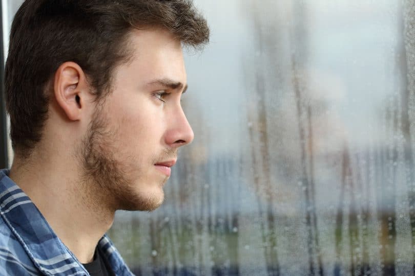depressão. Homem depressivo olhando para uma janela de vidro embaçada pela chuva.