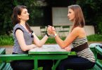 Duas mulheres em queda de braços sentadas em mesa de parque
