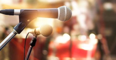 Foto close de dois microfones colocados em cima de um palco, representando a comunicação.