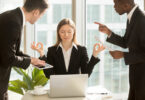 Mulher meditando em sua mesa de trabalho enquanto dois homens ao gritam ao redor dela.