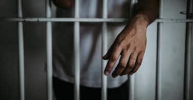 Mão de um homem preso por fora da cela