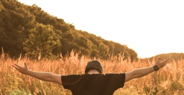 Homem de costas com braços abertos e campo ao fundo