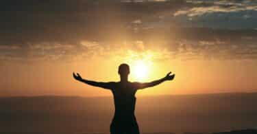 Silhueta de pessoa com braços abertos com pôr-do-sol ao fundo