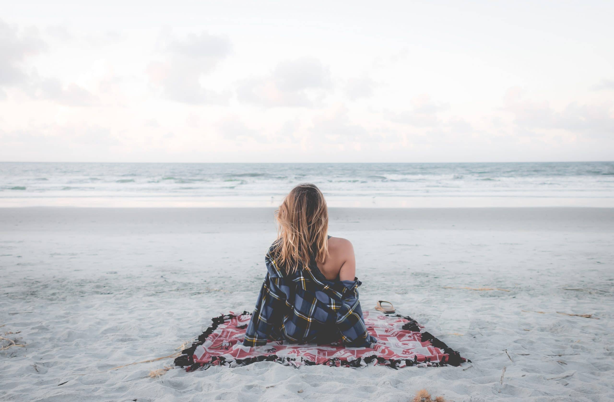 Mulher sentada de costas na praia 