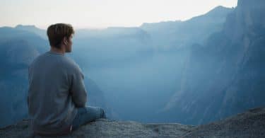 Homem sentado em montanha olhando para o horizonte