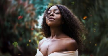 Mulher negra, jovem, com os cabelos naturais soltos ao vento, em meio de uma floresta.