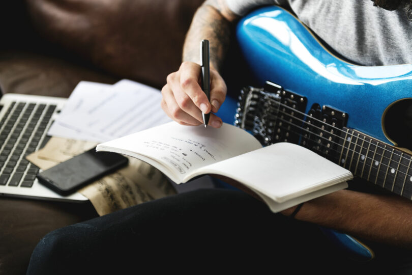 Homem com guitarra azul, escrevendo em um caderno