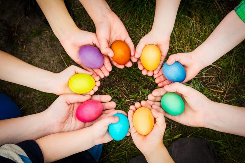 Mãos brancas segurando ovos coloridos.