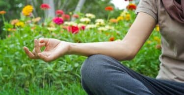 Pessoa sentada na grama, meditando, cercada por flores