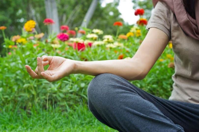 Pessoa sentada na grama, meditando, cercada por flores