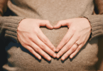 Mulher grávida fazendo símbolo de coração sobre sua barriga.