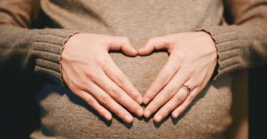 Mulher grávida fazendo símbolo de coração sobre sua barriga.