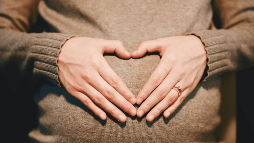 Mulher grávida fazendo símbolo de coração sobre sua barriga.