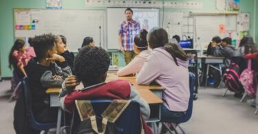 Sala de aula com alunos sentados e professor dando aula