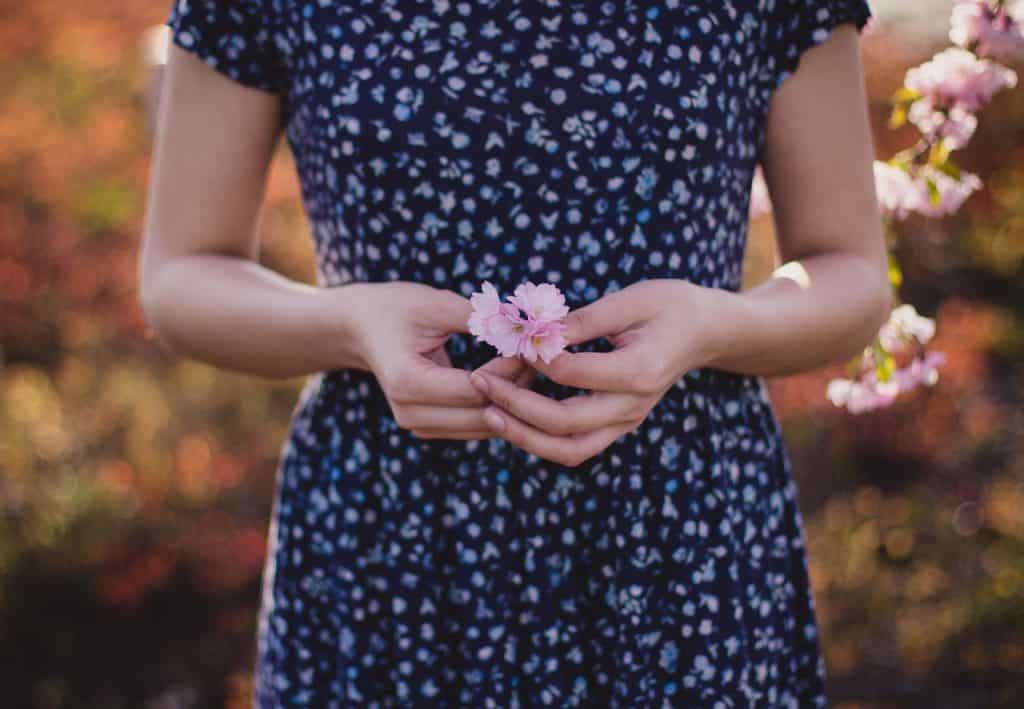 Mulher de vestido segurando uma pequena flor, em um parque.