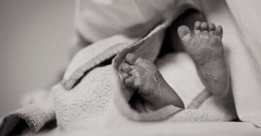 Foto em preto e branco dos pés de um bebê recém nascido, enrolado em um cobertor.
