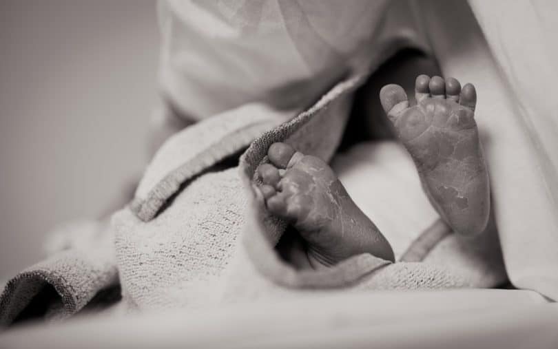 Foto em preto e branco dos pés de um bebê recém nascido, enrolado em um cobertor.