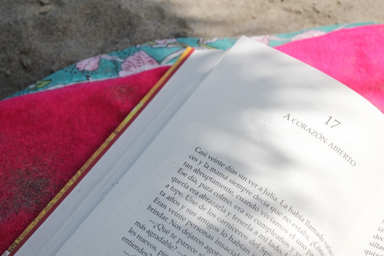 Livro aberto, com páginas brancas, colocado em cima de uma toalha rosa, no chão.