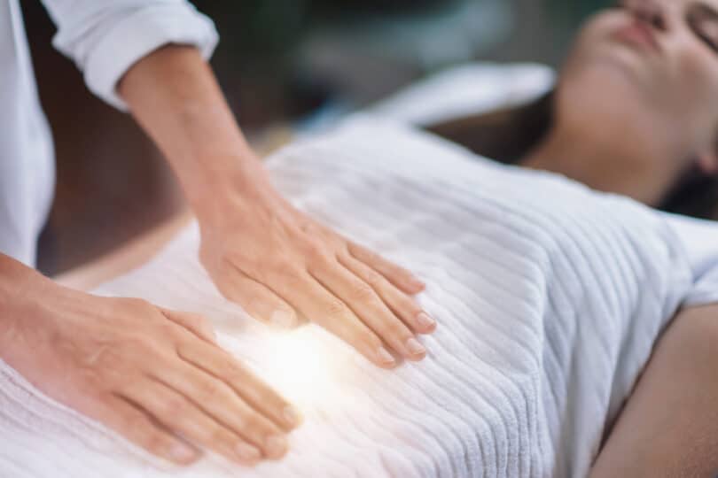 Mulher realizando reiki em outra. Há luz saindo das palmas das mãos.