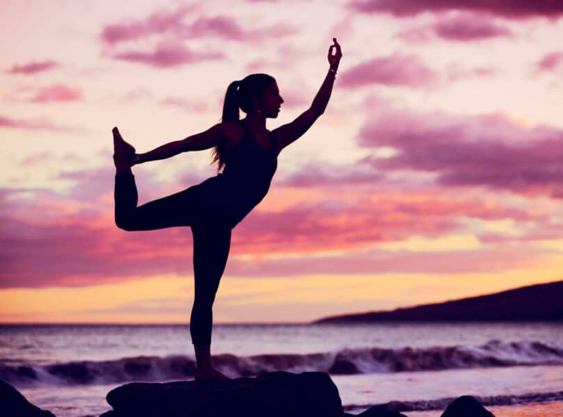 Silhueta de mulher praticando yoga com o céu roxo ao fundo.