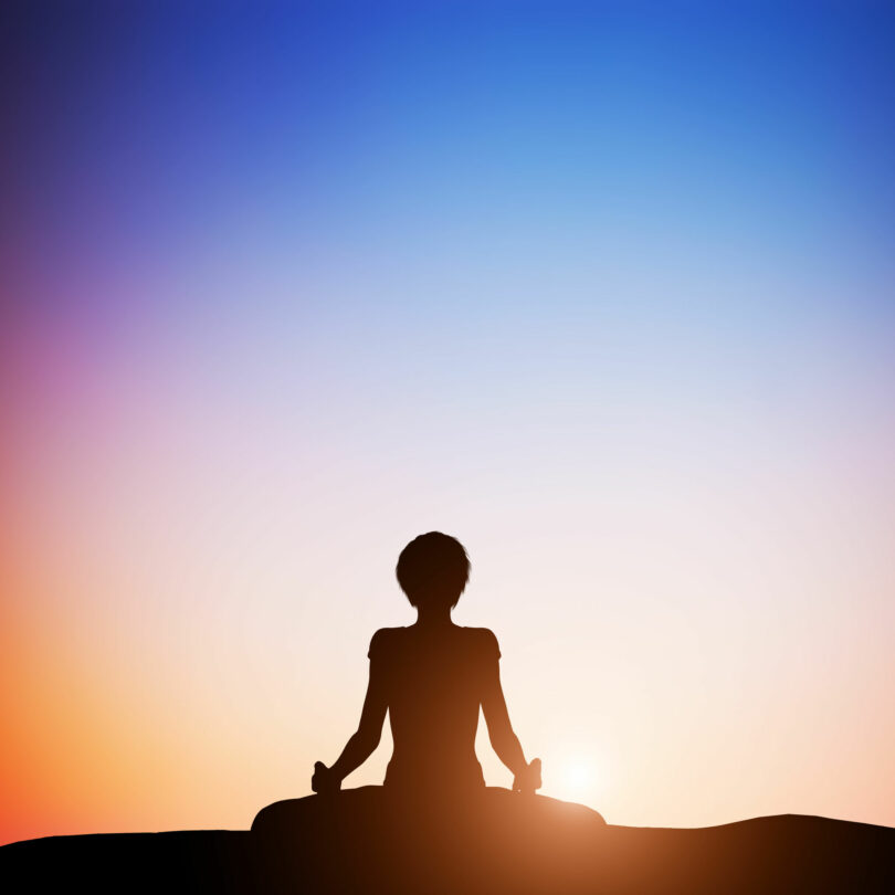 Silhueta de mulher sentada em posição de lótus, com as pernas cruzadas, meditando.