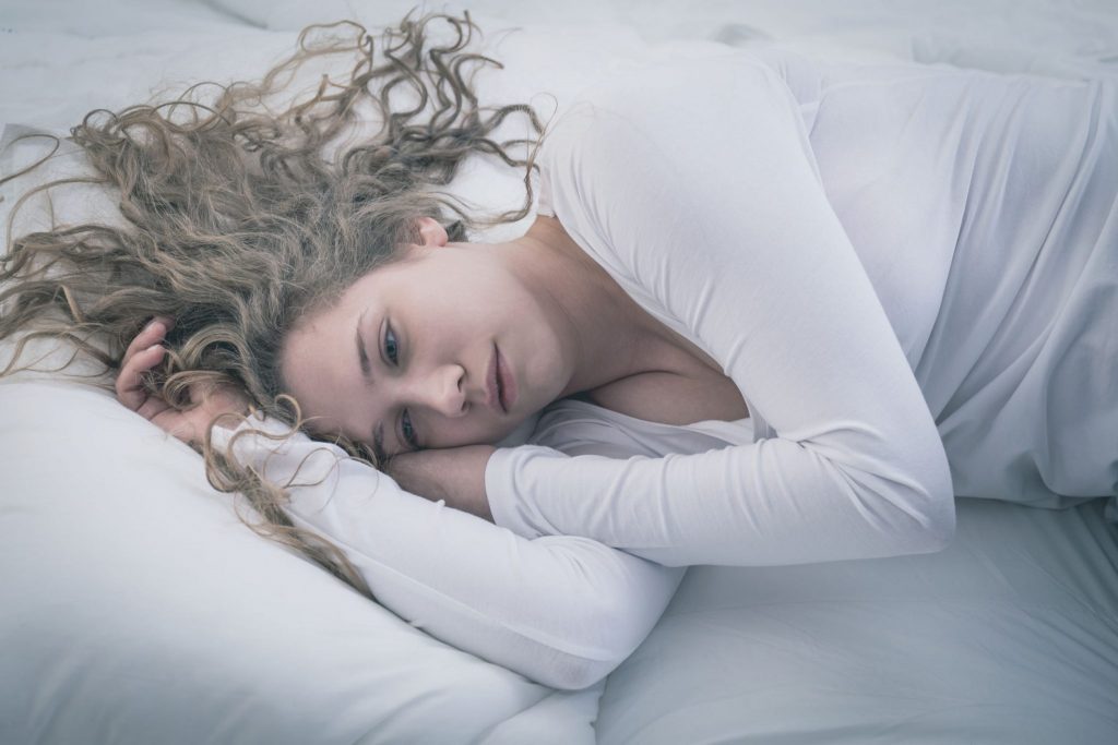 Mulher deitada com expressão triste e olhos de quem chorou recentemente.