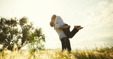 Casal se beijando com homem segurando mulher no colo no campo