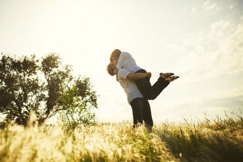 Casal se beijando com homem segurando mulher no colo no campo
