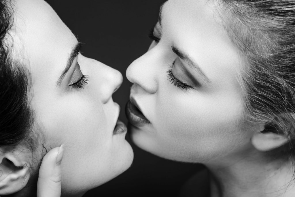 Casal de mulher se preparando para o beijo na boca. A imagem está em preto e branco. Sómente o rosto de ambas é visto na foto.
