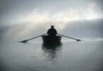 Foto de silhueta de pessoa em um barco, remando no meio do mar com o céu coberto por neblina.