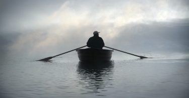 Foto de silhueta de pessoa em um barco, remando no meio do mar com o céu coberto por neblina.