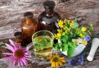 Caneca com chá herbal, vidros com extratos e plantas em cima de uma mesa de madeira.