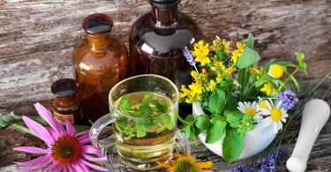 Caneca com chá herbal, vidros com extratos e plantas em cima de uma mesa de madeira.