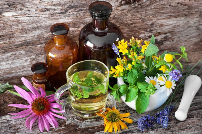 Caneca com chá herbal, vidros com extratos e plantas em cima de uma mesa de madeira.