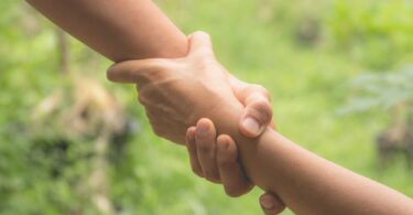 Duas mãos de pessoas diferentes se entrelaçam, simbolizando ajuda.